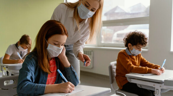 Niños con máscaras médicas que estudian en la escuela con el maestro