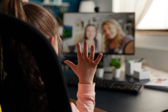 Niña o niño viendo una pantalla con la mano levantada saludando a quiénes están en esa pantalla