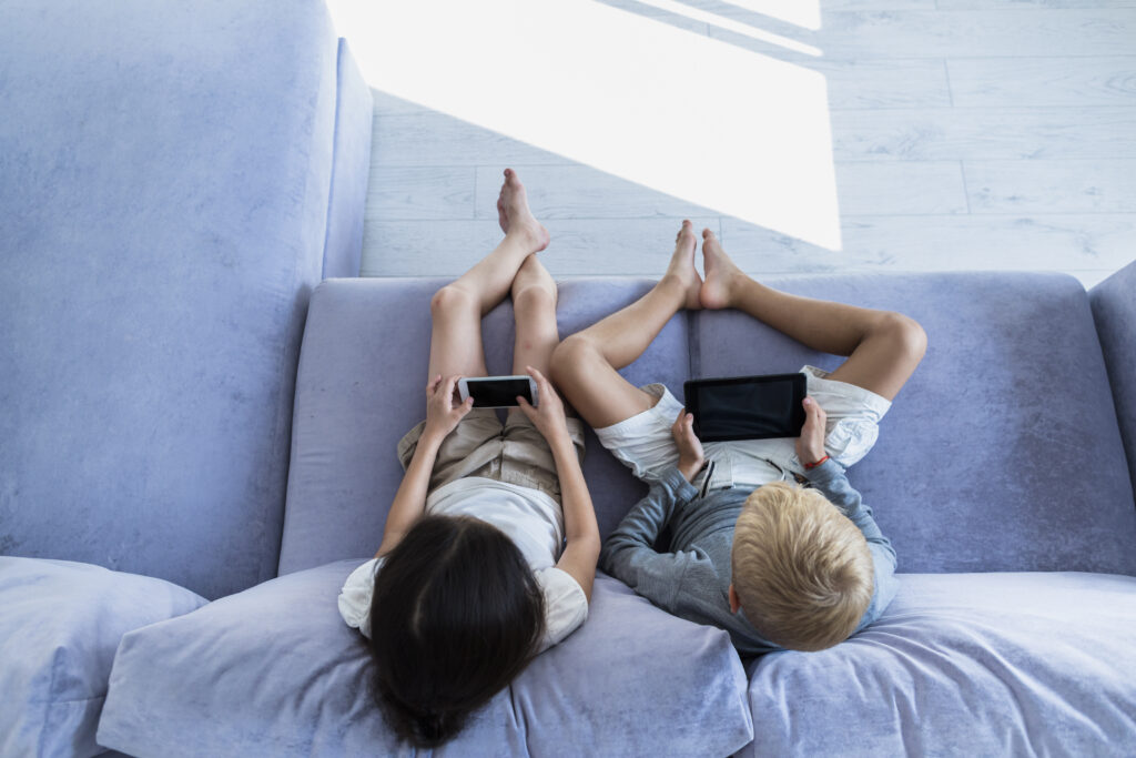 Niños sentados en un sofá usando dispositivos móviles.