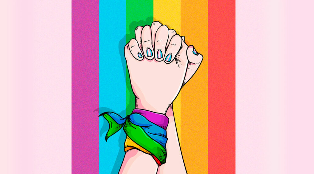 Manos entrelazadas con uñas pintadas y pañuelo del orgullo, con arco iris de fondo.
