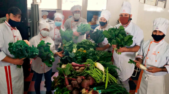 cocineros y cocineras posan junto a una mesa llena de verduras.