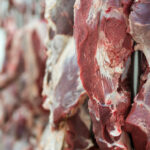 Primer plano de cortes cárnicos, con un trabajador de frigorífico desenfocado de fondo.