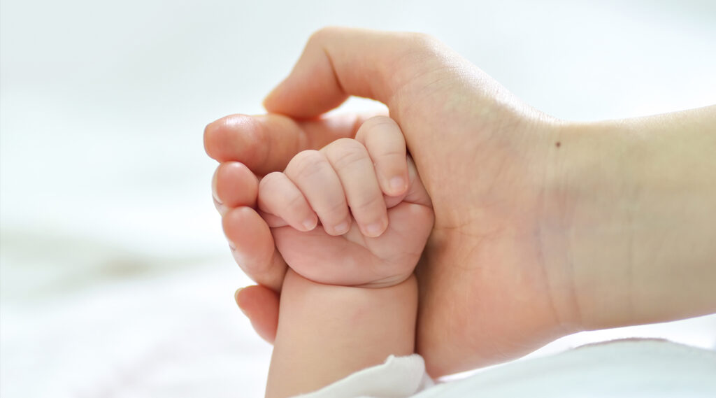 Mano de bebé sosteniendo mano de adulto.