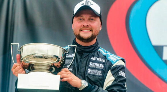 El piloto Joel Gassman posando sonriente con un trofeo.