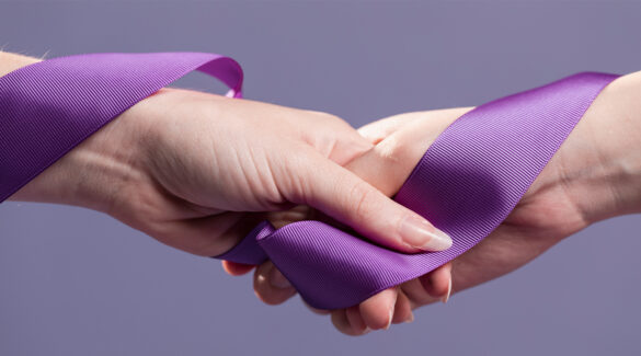 Manos femeninas entrelazadas con una cinta violeta.