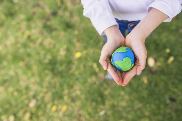 persona sosteniendo un planeta en escala - perspectiva desde arriba -fondo de pasto verde