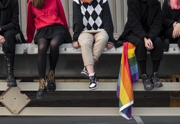 Foto de 4 Jóvenes sentados, uno de ellos con bandera de la diversidad
