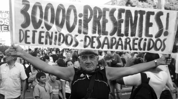 Un señor en una marcha sostiene una bandera con la frase: "treinta mil ¡presentes! detenidos desaparecidos"