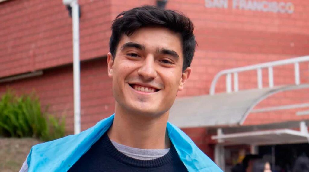 Augusto, estudiante de la facultad de ciencias de la educación, posando sonriente frente a la universidad de Colombia donde cursa como estudiante de intercambio.