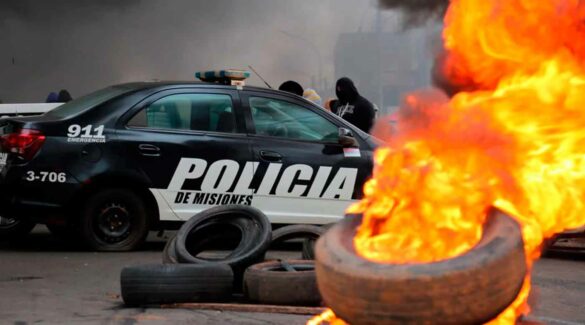 Auto de la policía misionera frente a una cubierta prendida fuego durante la protesta.