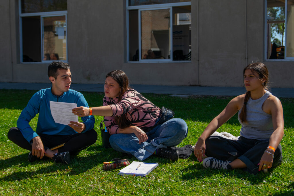 Foto de tres estudiantes sentados en el patio de la facultad.