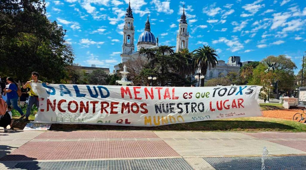 Personas sosteniendo una bandera que dice "La salud mental es que todos encontremos nuestro lugar".