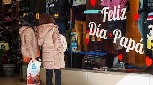 Dos mujeres mirando una vidriera con la leyenda "feliz día del padre"