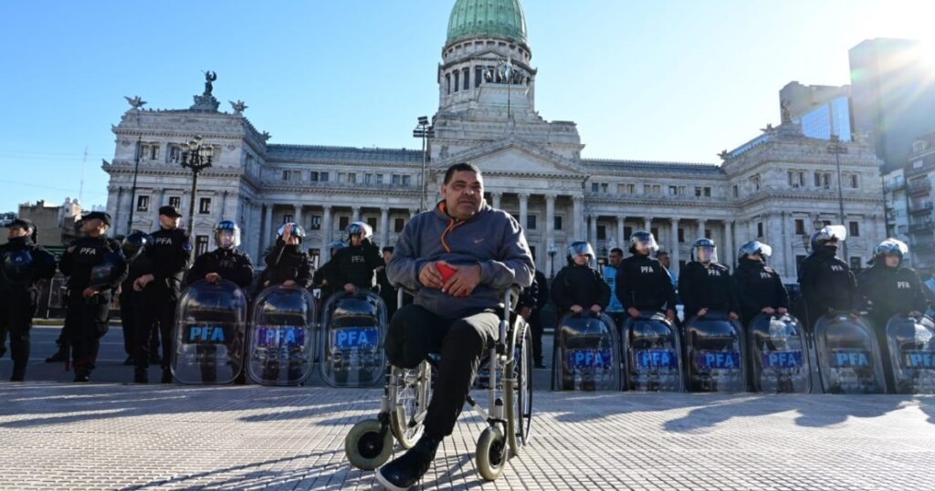 Hombre en silla de ruedas reclamando por el desfinanciamiento a las discapacidados y de fondo un cordón policial listo para reprimir