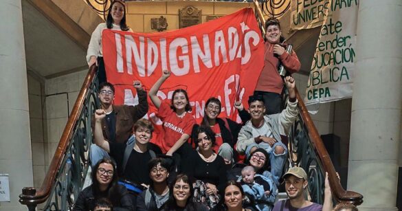 Militantes en una escalera sosteniendo una bandera roja con la leyenda "Indignadxs"